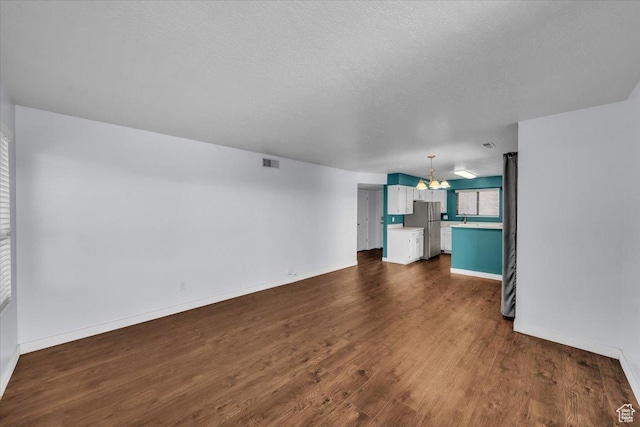 unfurnished living room featuring dark wood-type flooring, visible vents, a textured ceiling, and baseboards