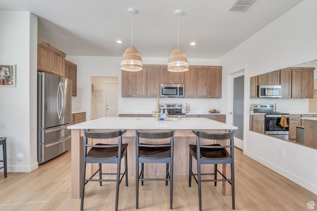kitchen with an island with sink, light wood-style flooring, light countertops, visible vents, and appliances with stainless steel finishes