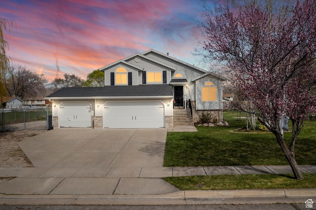 tri-level home with concrete driveway, an attached garage, a garage, a yard, and fence