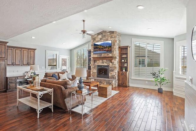 living area with dark wood-type flooring, a stone fireplace, lofted ceiling, and ceiling fan