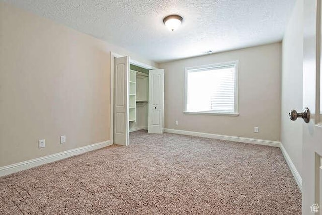 unfurnished bedroom with a textured ceiling, a closet, light colored carpet, and baseboards