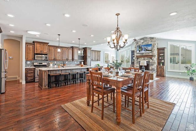 dining space with a stone fireplace, recessed lighting, a notable chandelier, and dark wood-style floors