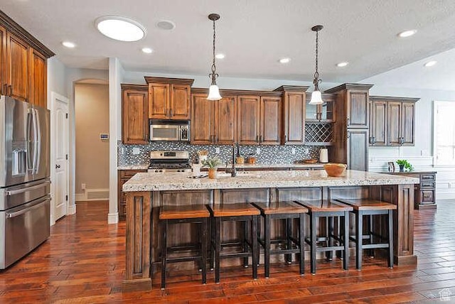 kitchen with stainless steel appliances, light stone counters, and dark wood finished floors