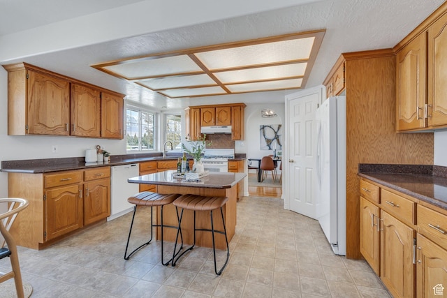 492 W 175 N, Orem, UT 84057 - kitchen featuring white appliances, brown cabinetry, under cabinet range hood, a sink, and a breakfast bar area