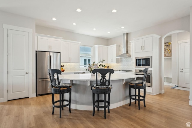 10713 S Lake Terrace Ave, South Jordan, UT 84009 - kitchen featuring a kitchen island, white cabinets, wall chimney exhaust hood, appliances with stainless steel finishes, and arched walkways
