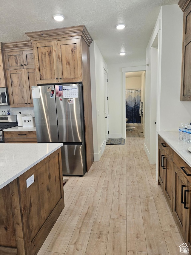 2345 E Cherry Ln, Layton, UT 84040 - kitchen with light wood-style flooring, a textured ceiling, light countertops, stainless steel appliances, and brown cabinets