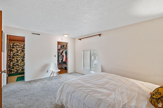 carpeted bedroom with a closet, a spacious closet, a textured ceiling, connected bathroom, and visible vents