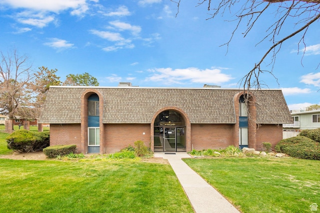 view of front of property featuring brick siding, a shingled roof, a front lawn, and mansard roof
