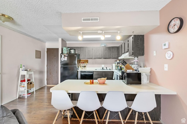 kitchen with a peninsula, light countertops, a textured ceiling, visible vents, and black appliances