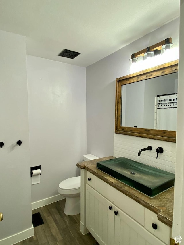 bathroom with vanity, visible vents, toilet, wood finished floors, and baseboards