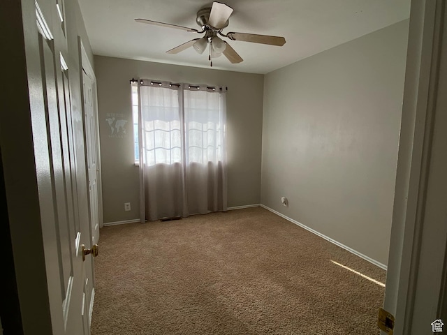 carpeted spare room featuring ceiling fan and baseboards