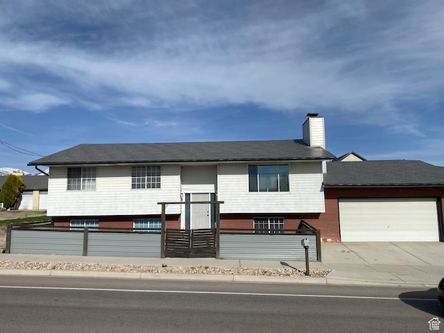 split foyer home with an attached garage, fence, driveway, and a chimney