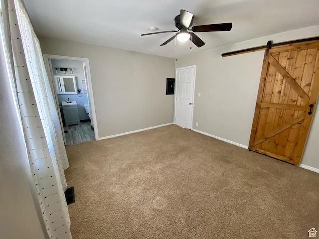 unfurnished bedroom featuring ensuite bath, electric panel, a barn door, carpet flooring, and baseboards