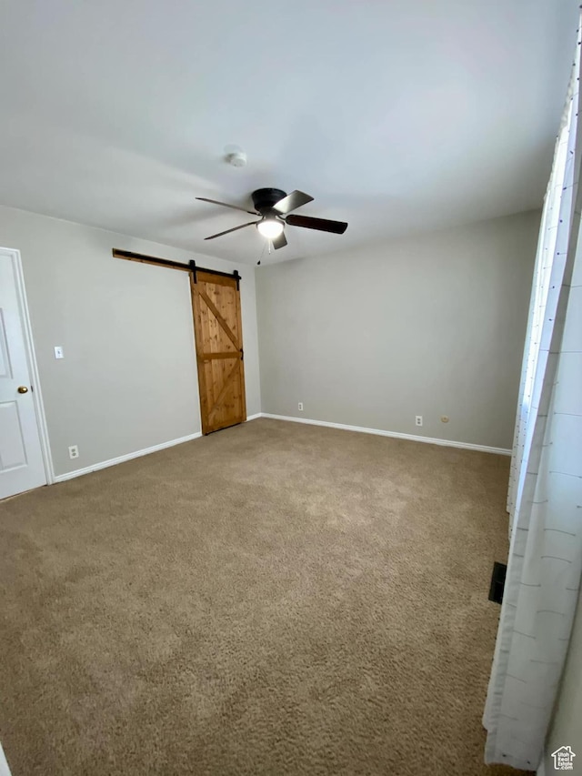 unfurnished bedroom with visible vents, baseboards, a barn door, ceiling fan, and carpet floors