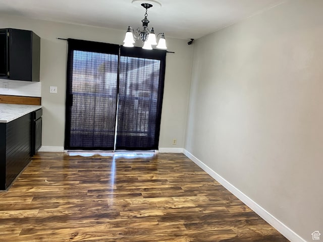unfurnished dining area with a chandelier, wood finished floors, and baseboards
