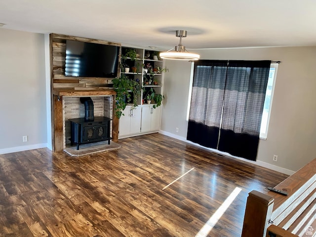 unfurnished living room featuring visible vents, a wood stove, wood finished floors, and baseboards