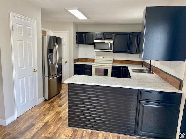 kitchen featuring light stone countertops, dark wood-type flooring, a peninsula, a sink, and stainless steel appliances