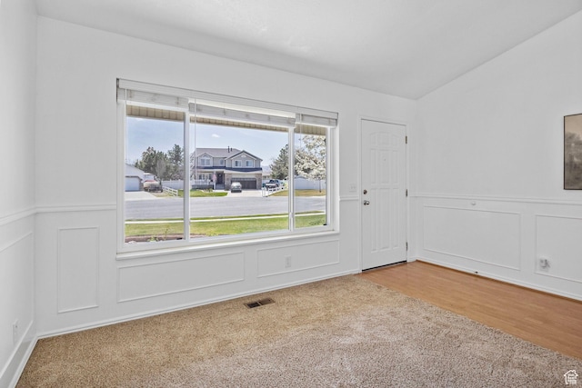 empty room featuring wood finished floors, a decorative wall, visible vents, and a wainscoted wall