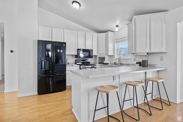kitchen with a kitchen breakfast bar, a sink, black appliances, a peninsula, and white cabinetry