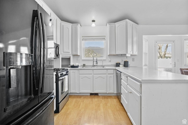kitchen with a sink, appliances with stainless steel finishes, a peninsula, and white cabinetry