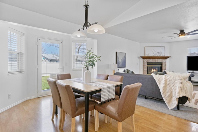 dining area with light wood-style floors, baseboards, a glass covered fireplace, and ceiling fan