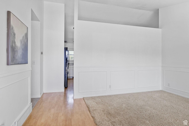 empty room with light wood-style floors, a wainscoted wall, and visible vents