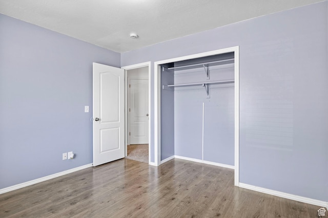unfurnished bedroom with baseboards, wood finished floors, and a closet
