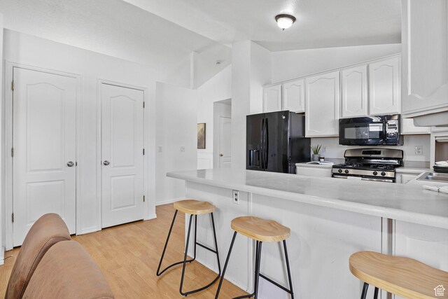 kitchen with a kitchen breakfast bar, vaulted ceiling, white cabinets, black appliances, and light wood-style floors