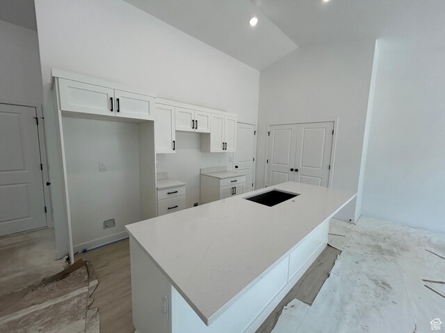 kitchen with white cabinets, high vaulted ceiling, light wood-type flooring, a center island, and baseboards