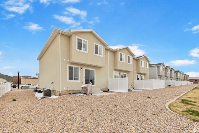 rear view of house featuring a residential view, central air condition unit, fence private yard, and stucco siding