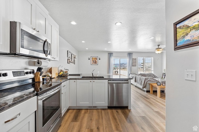kitchen featuring stainless steel appliances, a peninsula, light wood-style flooring, and a sink