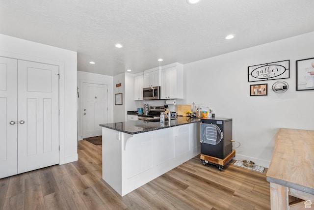 kitchen with light wood-type flooring, a peninsula, white cabinetry, dark stone counters, and stainless steel appliances