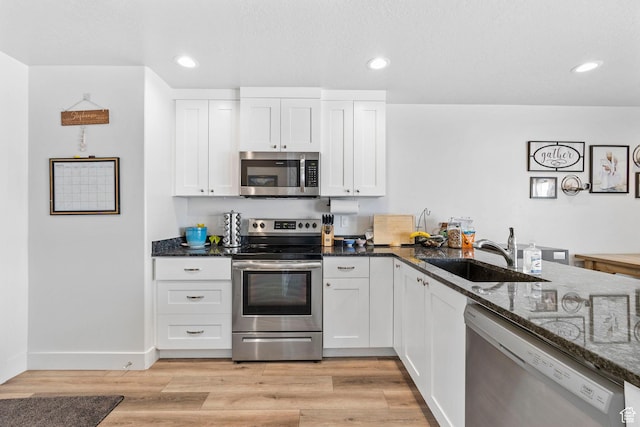 kitchen with dark stone countertops, light wood finished floors, a sink, and appliances with stainless steel finishes