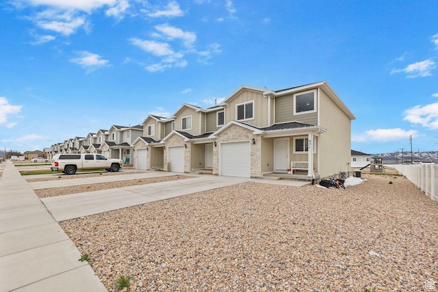view of property featuring stone siding, a garage, fence, concrete driveway, and a residential view