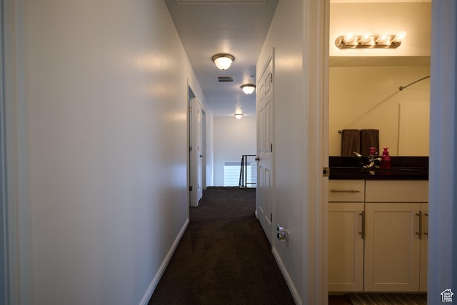 corridor featuring a sink, visible vents, baseboards, and dark colored carpet
