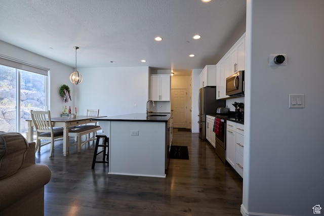 kitchen featuring recessed lighting, an island with sink, dark countertops, white cabinets, and appliances with stainless steel finishes