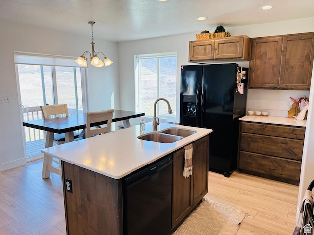 kitchen with light wood-style flooring, black appliances, a sink, light countertops, and a notable chandelier