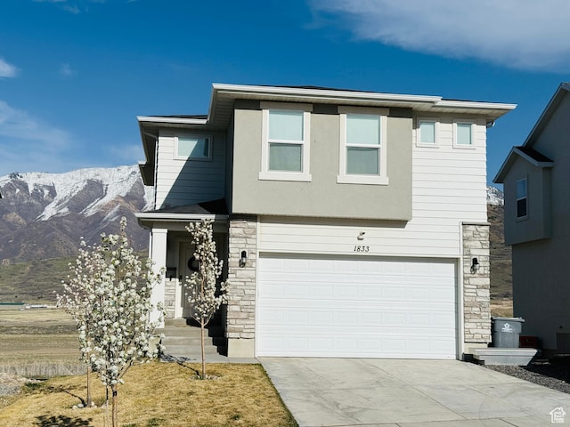 view of front facade featuring an attached garage, driveway, a mountain view, and stone siding