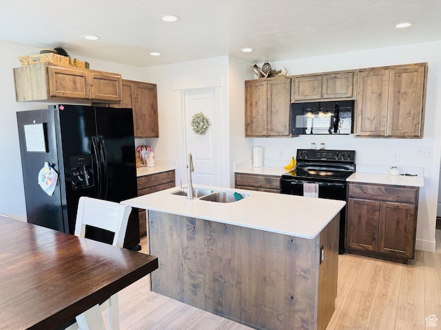 kitchen with a sink, light countertops, light wood-style flooring, and black appliances