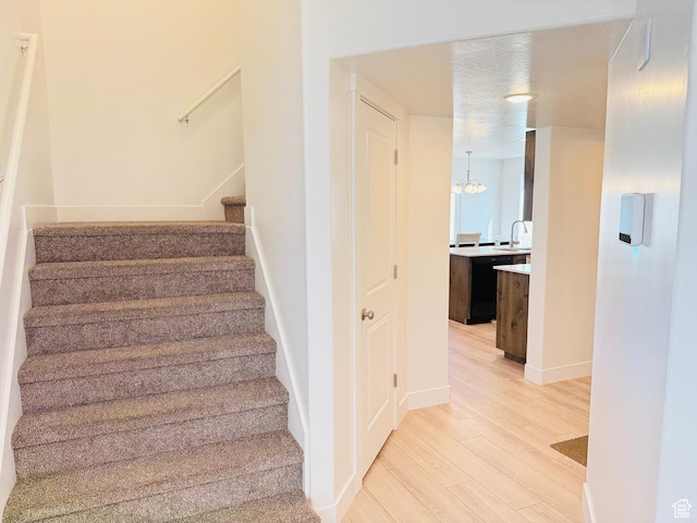 staircase featuring baseboards, an inviting chandelier, and wood finished floors