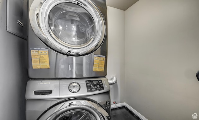 laundry area with dark tile patterned flooring, laundry area, stacked washer and clothes dryer, and baseboards