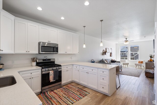 kitchen with open floor plan, appliances with stainless steel finishes, a peninsula, light wood-style floors, and white cabinetry