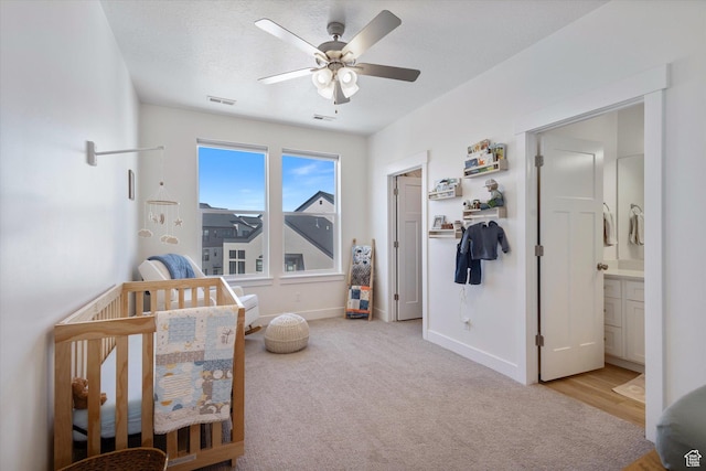 bedroom with ceiling fan, a nursery area, light colored carpet, visible vents, and baseboards