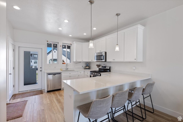 kitchen with light wood-style flooring, light countertops, a kitchen bar, stainless steel appliances, and a sink