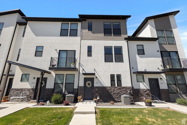 view of property featuring central AC unit, stucco siding, and stone siding