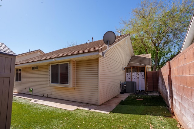 rear view of house featuring central AC unit, fence, and a yard