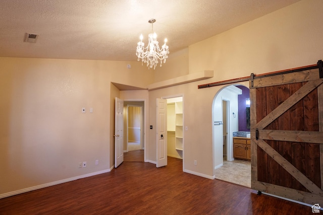unfurnished bedroom with wood finished floors, a walk in closet, arched walkways, a notable chandelier, and visible vents