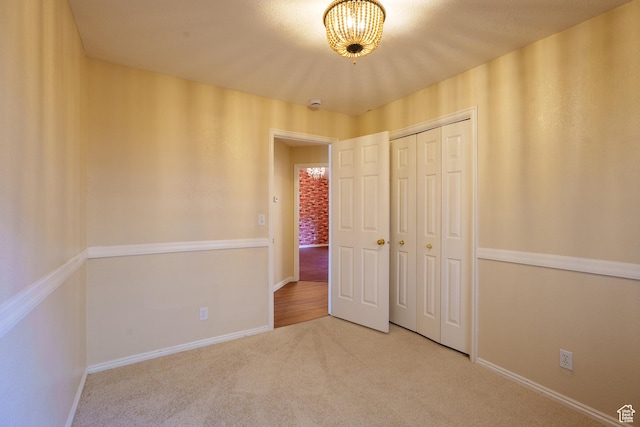 unfurnished bedroom featuring baseboards, a closet, a chandelier, and carpet