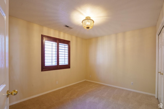 unfurnished room featuring baseboards, visible vents, light colored carpet, and a notable chandelier