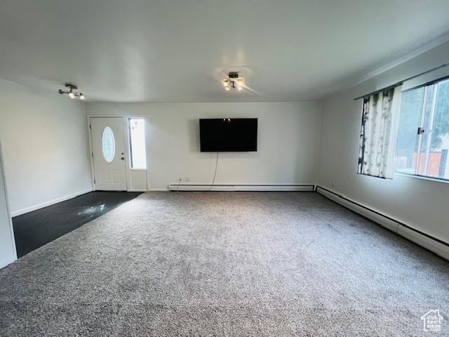 unfurnished living room with dark carpet, a baseboard heating unit, baseboards, and a wealth of natural light